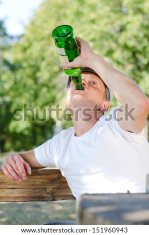 Boozer knocking back the alcohol gulping down the contents of a large green bottle of spirits as he sits outdoors in a park, low angle view