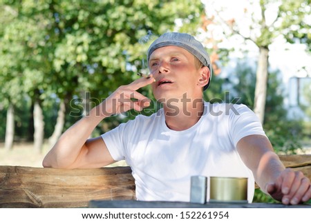 Low angle view of a good looking man sitting outdoors smoking at a rustic wooden table