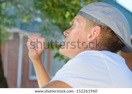Over the shoulder view of a trendy young man relaxing with a cigarette outdoors in the garden
