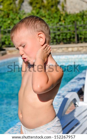 Young boy applying suntan lotion to his skin while standing in the hot summer sun at a swimming pool enjoying his vacation