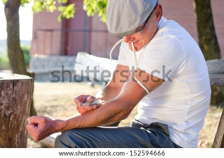 Caucasian addicted man injecting his tied arm intravenously with a dose of soluble heroin in the park