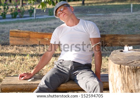 Addicted Caucasian man sitting on a bench in the park feeling side effects after injecting a drug dose intravenously