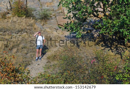 Man out backpacking on a mountain path standing with his hands to his eyes to shield the glare from the sun as he looks out over the view