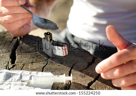 Hands of an addicted man while heating heroin with a lighter in order to fill the syringe