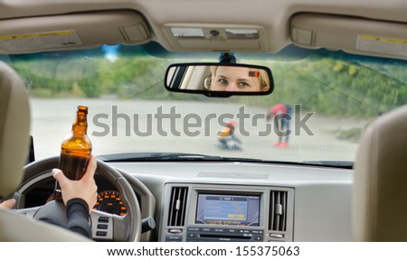 Road accident due to alcohol about to happen as a drunk female driver clutching her bottle of booze in one hand while driving approaches young children playing in the road