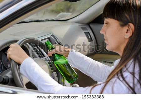 Female driver drinking and driving while grinning out of the side window as she clutches the steering wheel with her bottle of alcohol clasped in one hand