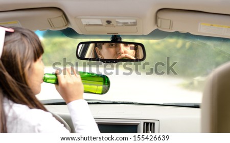 View from behind inside a car of a woman driver drink driving lifting the bottle to her lips and gulping down the alcohol as she steers the car