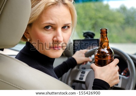 Aggressive drunk woman driver holding a bottle of alcohol turning round in the drivers seat to glare into the back passenger compartment at the viewer