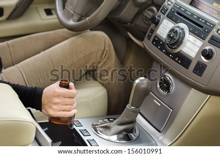 Woman alcoholic holding a bottle of booze in the car with it balanced in the console as she drives along posing a danger to other motorists
