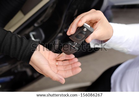 Close up view of the hands of a woman handing over a set of car keys to a second woman holding out her hand, conceptual image