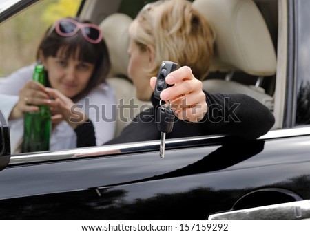 Woman driver reaching for a bottle of booze while holding the keys to her car out of the open window as though aware that her drinking would present a hazard to other motorists