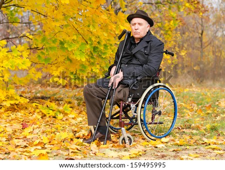 Portrait of a handicapped elderly gentleman in his wheelchair sitting in the autumn sun holding a pair of crutches as he enjoys the last warm weather of the season