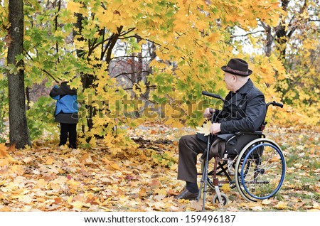 Disabled grandfather using a wheelchair taking care of his playing grandchild outdoors in the forest in the autumn