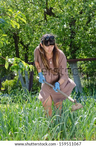 Attractive women working in the vegetable garden hoeing the weeds amongst the plants as she strives to become self-sufficient in feeding her family