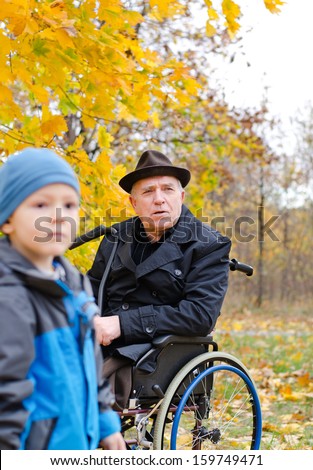 Disabled grandfather in a wheelchair and grandchild in the forest during autumn