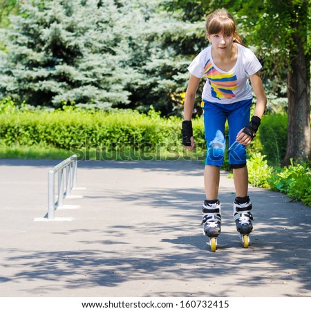 Young teenage girl practising her roller skating approaching the camera on her roller blades crouched forwards with a look of concentration in a rural skate park with copyspace