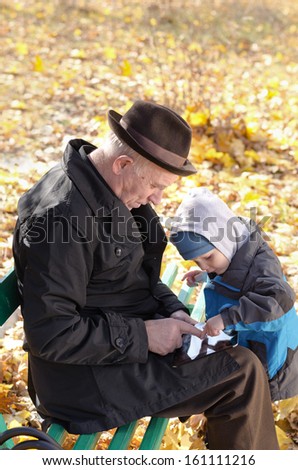 Grandfather and grandson sharing a tablet-pc surfing the internet together as they enjoy a day out in the fresh air at the park on a cold autumn day