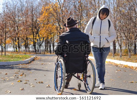Attractive middle-aged woman in a hooded top standing talking to a disabled man in a wheelchair
