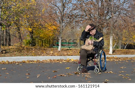 Lonely handicapped man in a wheelchair parked in the street with a bag of groceries on his lap waiting for someone to come and assist him