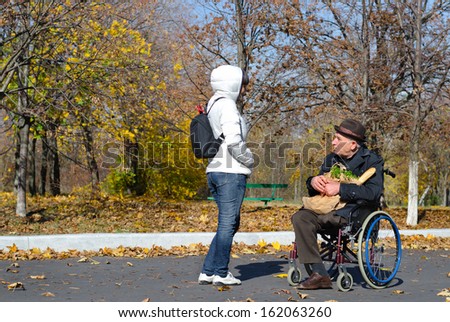 Handicapped senior man in a wheelchair stopping in the street to chat to a woman as he does his grocery shopping