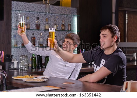 Two young men raising their beers in a toast cheering as they celebrate with friends in the pub