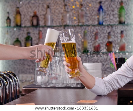 Two men toasting each other with their beers clinking their glasses over the counter as they celebrate together