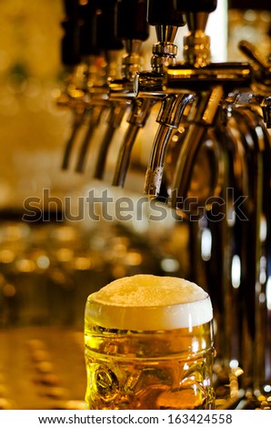 Close Up View Of A Tankard Of Beer With A Frothy White Head Standing On A Bar Counter In A Pub With Selective Focus To The Glass
