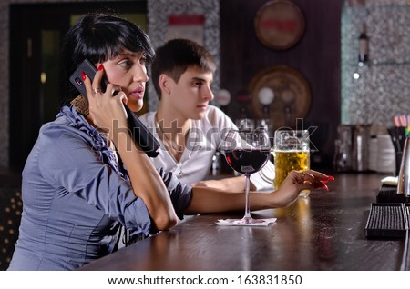 Two friends relaxing together drinking at the bar with a woman talking on a mobile phone with a serious expression and a large glass of red wine in front of her