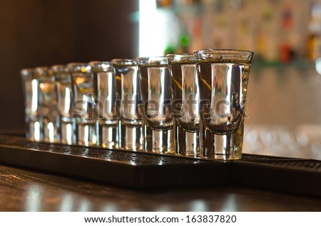 Row of clean shiny glasses lined up on a bar counter in a nightclub ready for the barmen to use to serve alcoholic beverages, oblique row with shallow dof