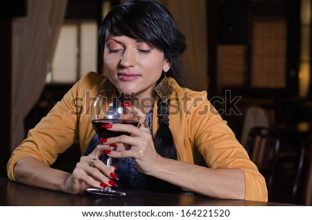 Mysterious fancy brunette young woman thinking while holding a glass of red wine at the bar