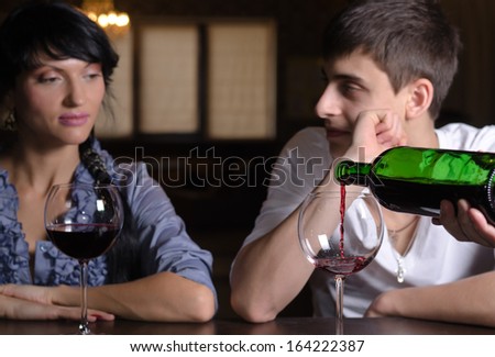 Young couple enjoying a glass of wine together at the bar in a nightclub with a male hand pouring wine from the bottle in the foreground