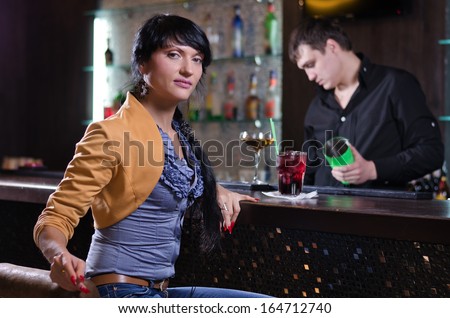 Portrait of a beautiful brunette independent young woman relaxing alone with a cocktail at the bar in a fancy location