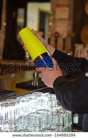 Hands of a barman mixing a cocktail in a colourful cocktail shaker standing behind the counter loaded with clean glassware