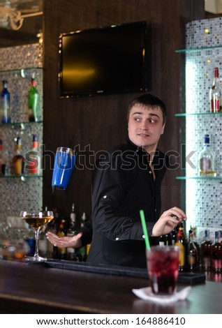 Barman serving a customer in a nightclub looking round attentively as someone places an order for a drink