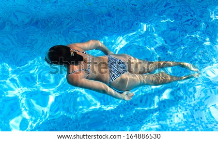 View from above of a woman in a bikini swimming face down in a turquoise blue pool in cool inviting sparkling water enjoying a summer vacation