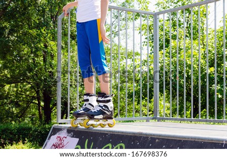 Legs of a young roller skater wearing rollerblades balanced on a cement ramp at the skate park ready to launch off for speed and height