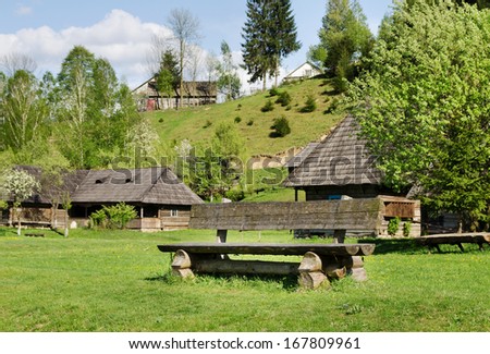 Rustic wood cabins with wooden shingles on their roofs scattered across a lush green mountain slope with a timber table and bench in the foreground for tourist accommodation while on vacation