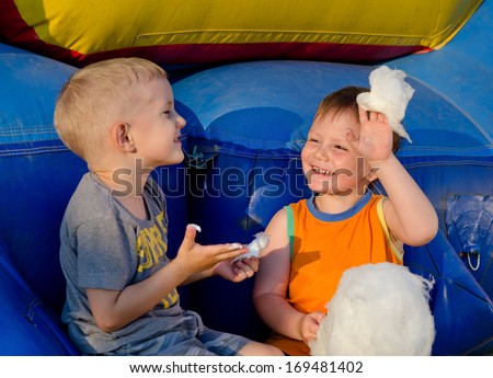 Two boys laughing together in the summer sunshine as they share a sticky serving of cotton candy or candy floss made from spun sugar on a stick