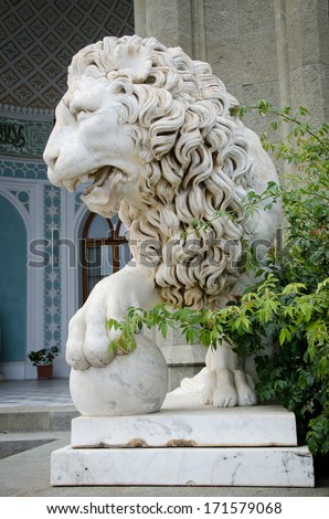 Beautifully carved naturalist stone lion statue with his paw resting on a sphere standing guard outside a historical building, closeup of the face of the lion