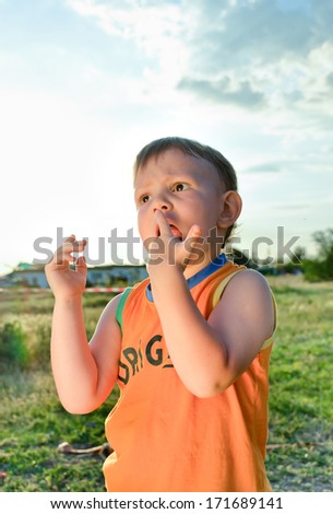 Young boy eating a stick of candy flass or cotton candy made from sticky spun sugar with obvious delight as he anticipates the next mouthful, standing in a rural environment backlit by the sun
