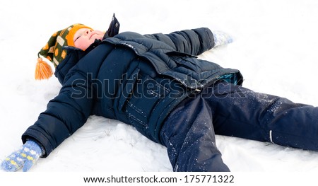 Happy little boy making snow angels in the snow lying on his back with his arms and legs outstretched with a smile of enjoyment