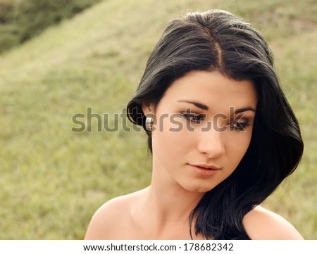 Beautiful amused young woman with long tousled dark brown hair grinning at the camera as she poses outdoors