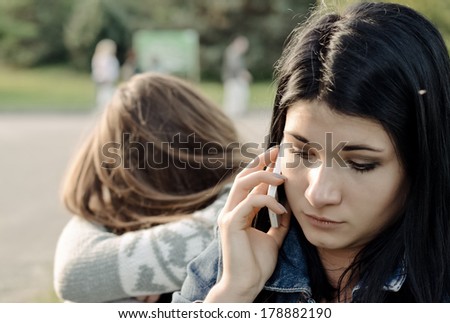Beautiful young woman chatting on her mobile phone listening to the conversation with a concerned expression while her friend waits in the background
