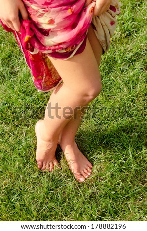 High angle view of a pair of sexy shapely barefoot female legs posing on green grass as she holds aside the fabric of her long skirt