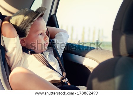 Little boy in a child safety seat sitting patiently in the back of a car with his hands behind his head staring out of the window