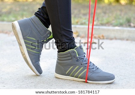 Feet of a woman athlete with a torsion rope or skipping rope gripped under the sole of her foot as she prepares to work out outdoors on a road in a park