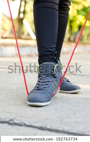 Feet of a woman athlete with a torsion rope or skipping rope gripped under the sole of her foot as she prepares to work out outdoors on a road in a park