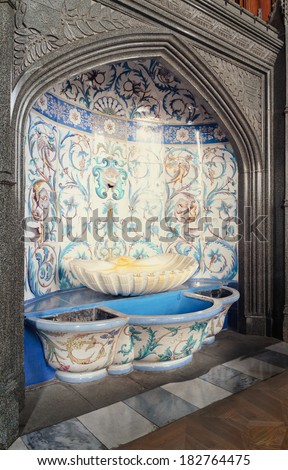 Historical ornate tiled font with a pretty blue arabesque pattern inset into a wall under a Gothic arch