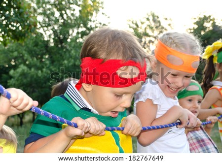 Young boy enjoying a tug of war at a party peering over the rope with a look of amazement on his face watched by his laughing young sister