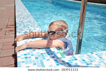 Small boy clambering out of a swimming pool onto the mosaic surround goggles and buoyancy jacket